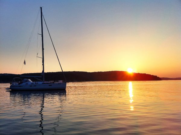 Man sieht ein Segelboot mit einem Sonnenuntergang im Hintergrund