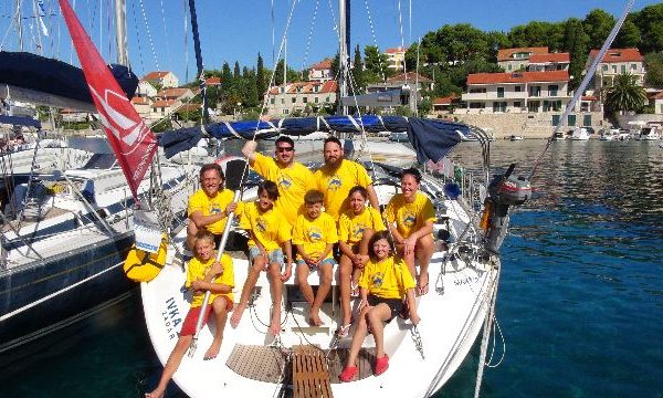 Man sieht eine Segelcrew mit gelben T-shirts auf ihrem Boot sitzen